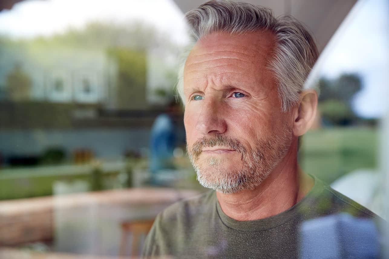 Man looking out window with worried look on his face