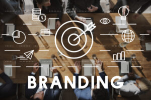 Overhead view of people meeting at a table, with the word BRANDING and white icons illustrating marketing concepts. Highlights from Brand Identity 101: What It Is and Why Your Business Needs It are visually represented in the scene.